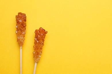 Photo of Wooden sticks with sugar crystals and space for text on yellow background, flat lay. Tasty rock candies