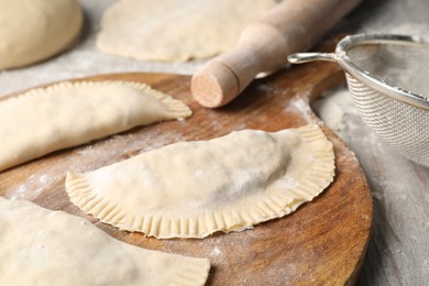 Photo of Raw chebureki with tasty filling and rolling pin on wooden table, closeup