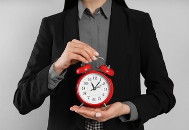 Businesswoman holding alarm clock on light grey  background, closeup. Time management