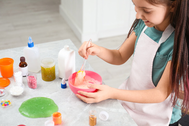 Little girl mixing ingredients with silicone spatula at table indoors, closeup. DIY slime toy
