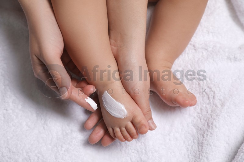 Photo of Mother applying moisturizing cream onto her little baby's skin on white towel, closeup