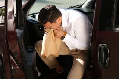 Man with paper bag suffering from nausea in car