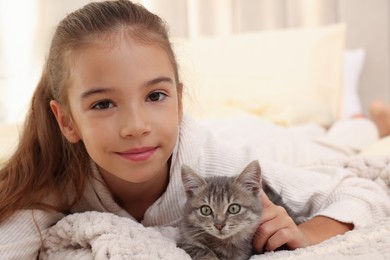 Cute little girl with kitten on white blanket at home. Childhood pet