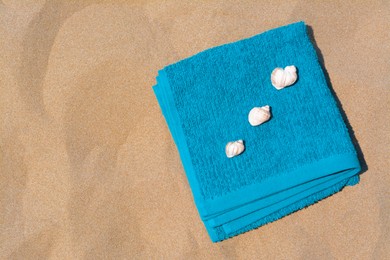 Folded soft blue beach towel with seashells on sand, flat lay. Space for text