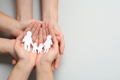 People holding paper family cutout on light grey background, top view. Space for text