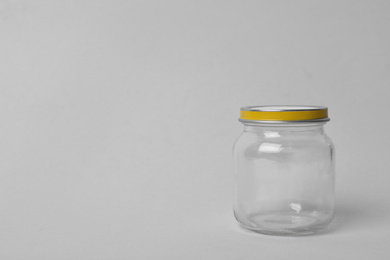 Closed empty glass jar on light background, space for text