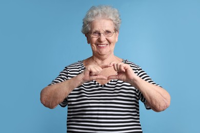 Elderly woman making heart with her hands on light blue background