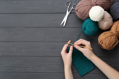 Woman crocheting with teal thread at grey wooden table, top view. Space for text