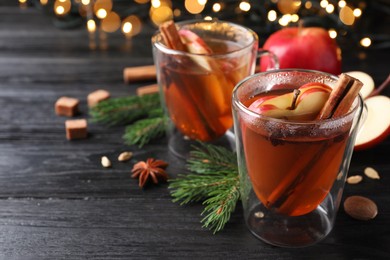 Aromatic hot mulled cider on black wooden table. Space for text