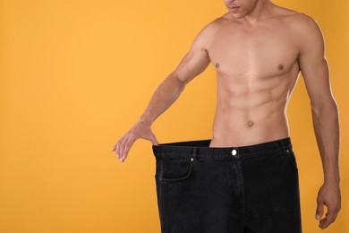 Shirtless man with slim body wearing big jeans on yellow background, closeup. Space for text