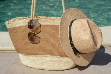 Stylish bag, sunglasses and hat near outdoor swimming pool on sunny day, closeup. Beach accessories