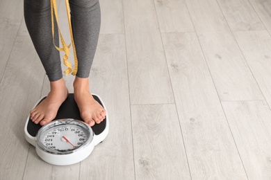 Woman with tape standing on scales indoors, space for text. Overweight problem