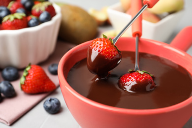 Dipping strawberries into fondue pot with chocolate on table, closeup