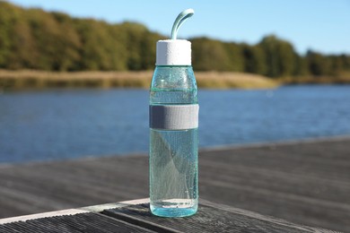 Glass bottle with water on wooden pier near river outdoors