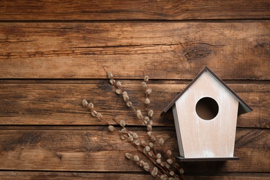 Beautiful bird house and willow branches on wooden background, flat lay. Spring composition with space for text