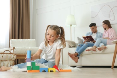 Little girl playing with colorful blocks while her parents resting on sofa at home. Floor heating concept