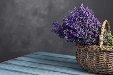 Photo of Beautiful fresh lavender flowers in wicker basket on wooden table against grey background. Space for text