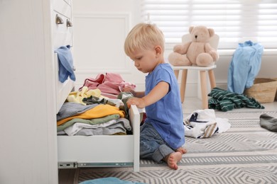 Cute little boy playing with clothes in dresser's drawer at home