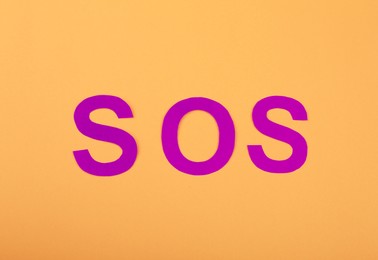 Abbreviation SOS made of paper letters on orange background, top view
