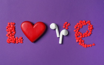 Word Love made with sprinkles, red heart and modern earphones on purple background, flat lay. Listening music songs