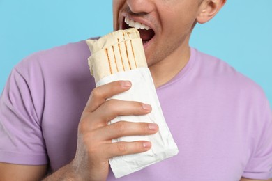 Photo of Man eating delicious shawarma on turquoise background, closeup