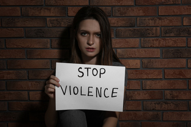Photo of Abused young woman with sign STOP VIOLENCE near brick wall