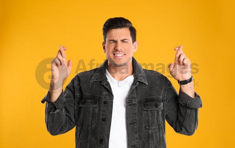 Man with crossed fingers on yellow background. Superstition concept