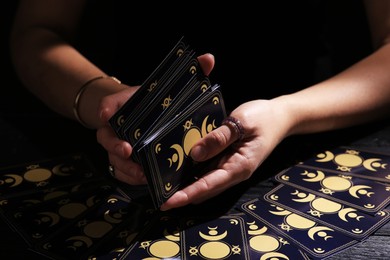 Photo of Soothsayer shuffling tarot cards at table in darkness. Fortune telling