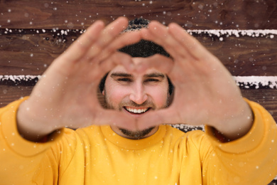 Young man making heart with his hands near wooden wall.  Winter vacation