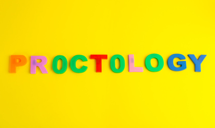Word PROCTOLOGY made of colorful letters on yellow background, top view. Hemorrhoid problems