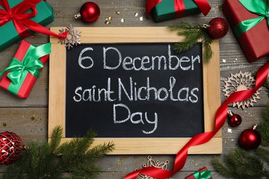 Blackboard with text 6 December Saint Nicholas Day, gift boxes and festive decor on wooden table, flat lay