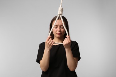 Depressed woman with rope noose on light grey background
