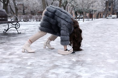 Young woman trying to stand up after falling on slippery icy pavement in park