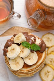 Photo of Tasty pancakes with sliced banana served on wooden board, top view