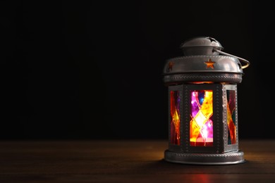 Decorative Arabic lantern on wooden table against black background, space for text