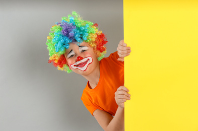 Preteen boy with clown wig looking out of yellow banner on light grey background, space for text. April fool's day