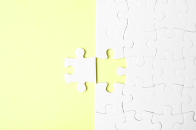 Blank white puzzle with separated piece on yellow background, flat lay