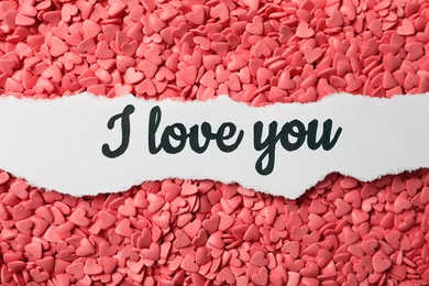 Handwritten message I Love You on pink heart shaped sprinkles, top view