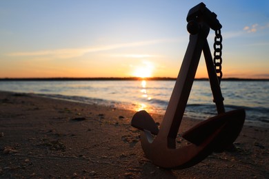 Photo of Wooden anchor on shore near river at sunset