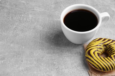 Photo of Tasty frosted donut and cup of coffee on light grey table, space for text
