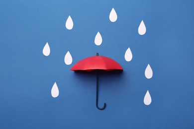 Photo of Mini umbrella and paper raindrops on blue background, flat lay
