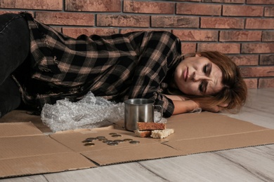 Poor homeless woman lying on floor near brick wall