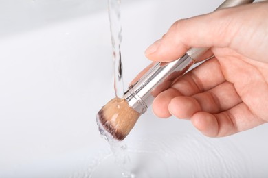 Woman washing makeup brush under stream of water in sink, closeup