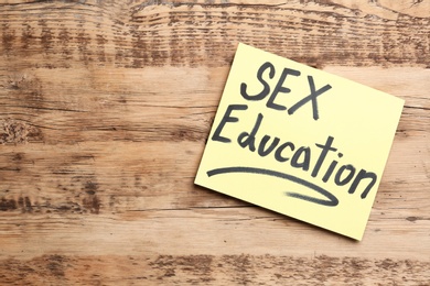 Note with phrase "SEX EDUCATION" on wooden background, top view. Space for text