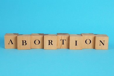 Word Abortion made of wooden cubes on light blue background