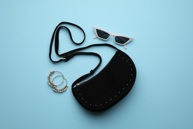 Stylish woman's bag, sunglasses and earrings on light blue background, flat lay
