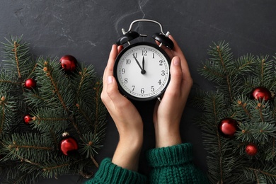 Photo of Woman with alarm clock near Christmas decor on black slate background, top view. New Year countdown