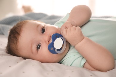 Cute little baby with pacifier on bed at home