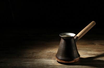Beautiful copper turkish coffee pot on wooden table against dark background, space for text