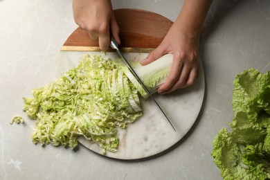 Woman cutting fresh Chinese cabbage at light grey table, top view